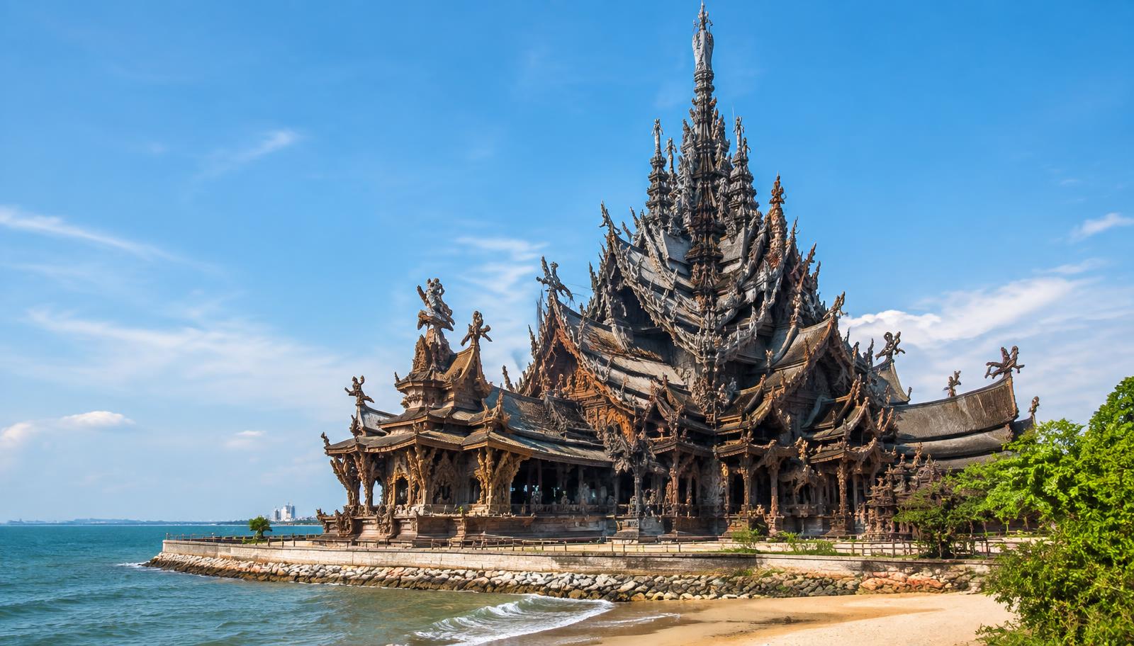 The intricately carved wooden spires of the Sanctuary of Truth beside the sea in Pattaya under a blue sky