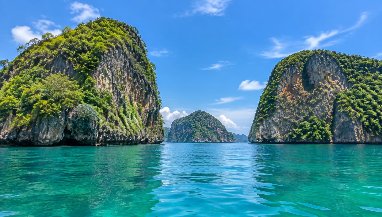 Limestone karst islands covered in green vegetation rising from calm emerald water in the Andaman Sea