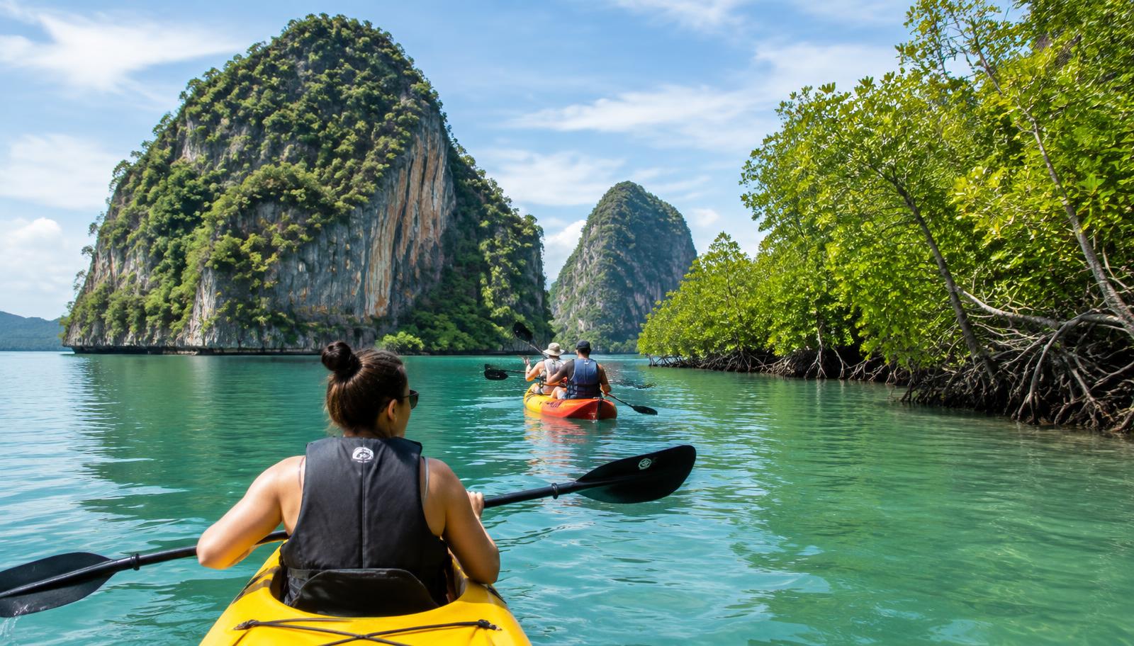 Travelers kayaking past mangroves and limestone cliffs in Krabi