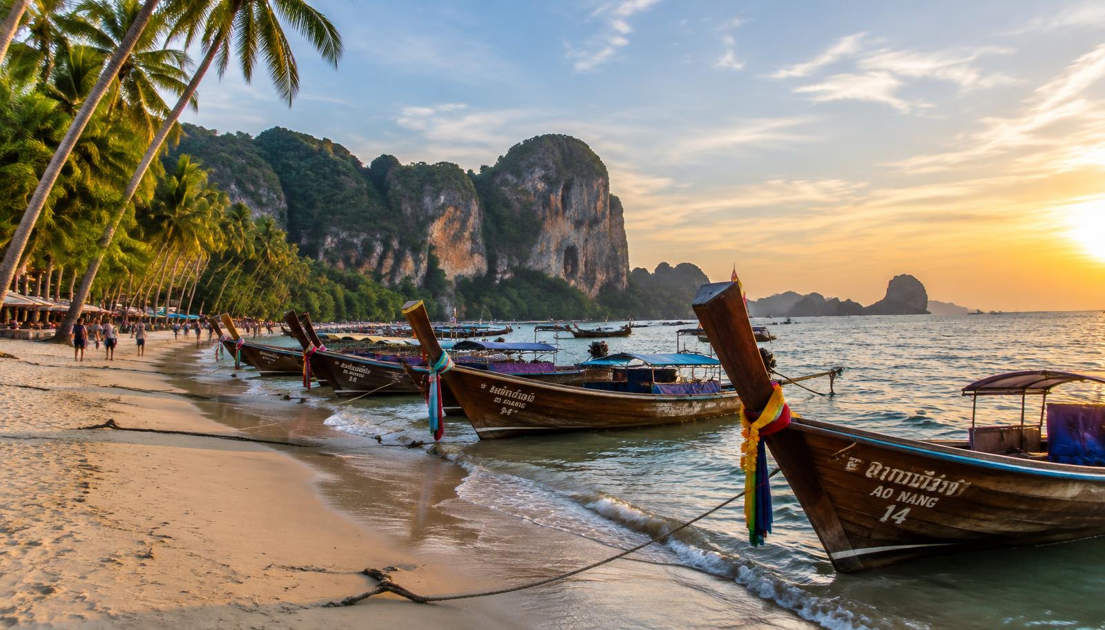 Longtail boats lined up on Ao Nang beach at sunset with limestone cliffs behind